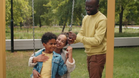 African-American-Boy-Swinging-on-Swing-with-Mother-on-Family-Walk-in-Park